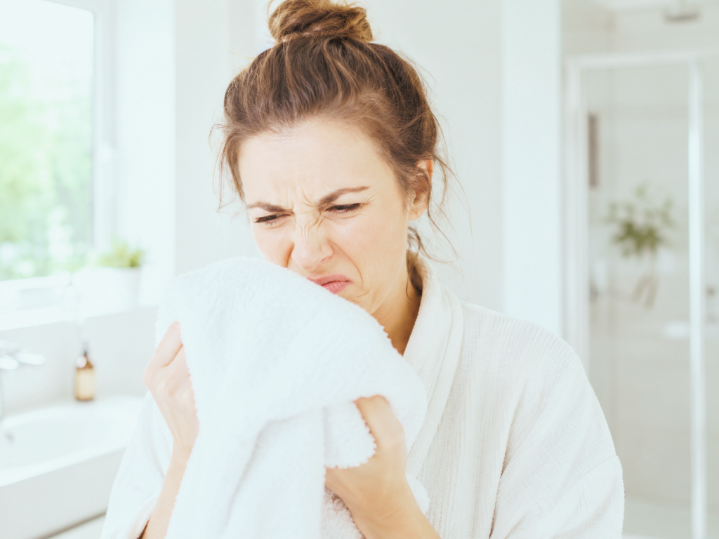 person smelling musty mildew odor from freshly washed white bath towel