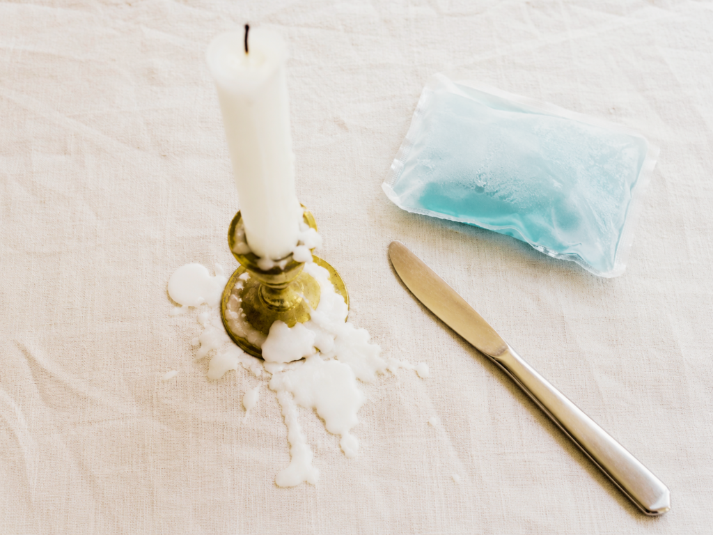 candle wax dripped on linen tablecloth with butter knife and ice pack nearby