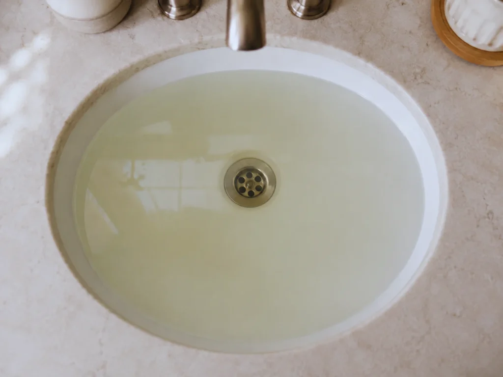 standing water in bathroom sink indicating clogged drain that needs to be unclogged